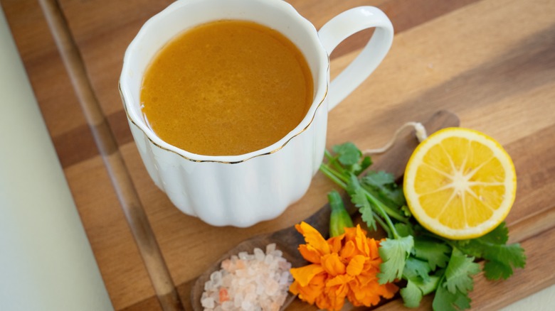 A cup of bone broth with aromatics alongside it