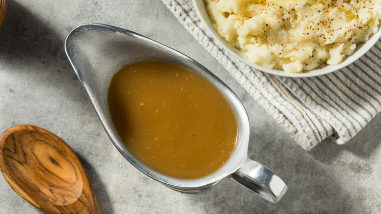 A gravy pot filled with brown gravy next to mashed potatoes