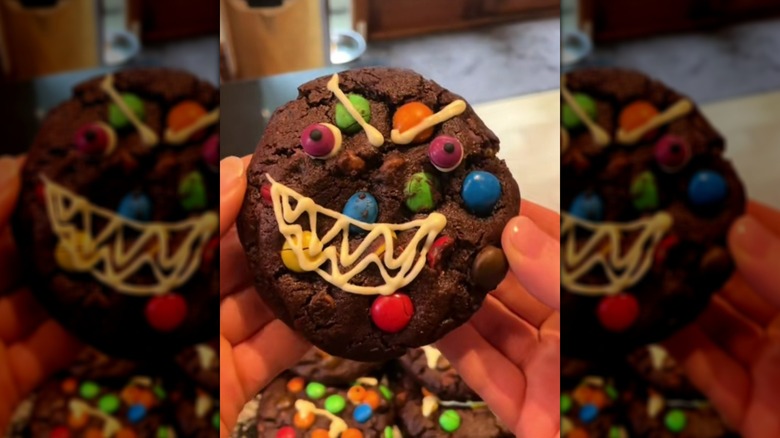 Hands holding M&M chocolate cookie, decorated with a monster face