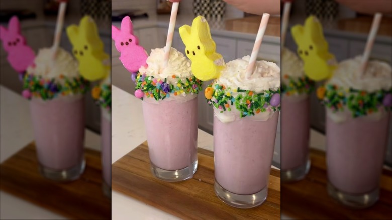 Two Easter-themed milkshakes in glasses, topped with whipped cream, sprinkles, and marshmallow Peeps