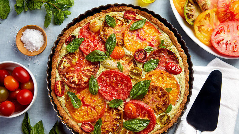 Tomato, basil, and, ricotta tart surrounded by fresh tomatoes, salt, and herbs
