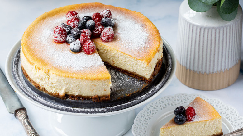 Sliced ricotta cheesecake on cake stand, topped with berries and dusted with powdered sugar