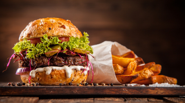 Burgers with lettuce, oozing cheese, tomatoes, and pickles, served with fries on a wooden board