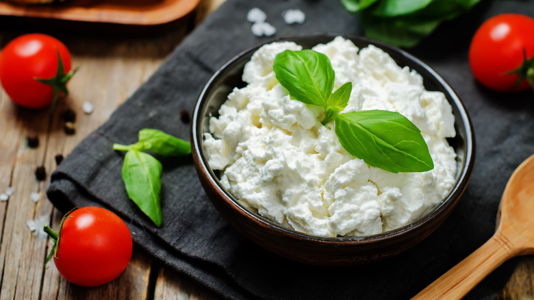 Ricotta cheese in black bowl with fresh basil and cherry tomatoes