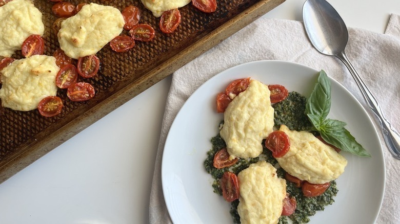 Ricotta gnudi served on plate with pesto and roasted tomatoes next to a sheet pan