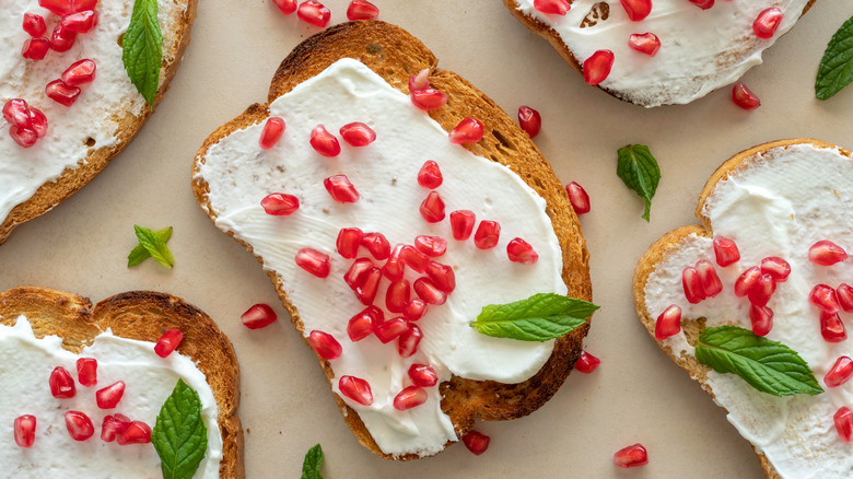 Top view of whipped ricotta on slices of toast with pomegranate seeds and fresh mint leaves