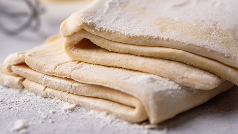 Pile of folded puff pastry dough dusting with flour on work surface