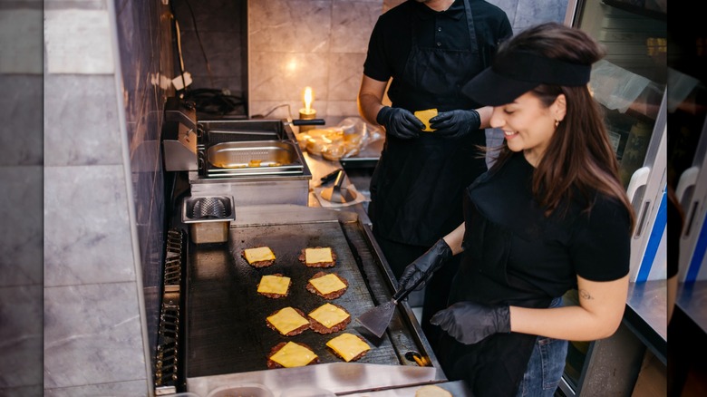 Smiling woman flipping cheeseburgers behind a fast food grill