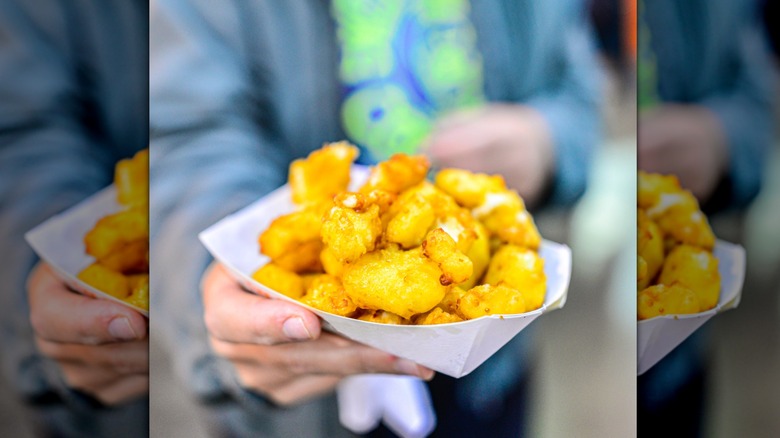 Hand holding up a white container filled with golden, deep-fried cheese curds
