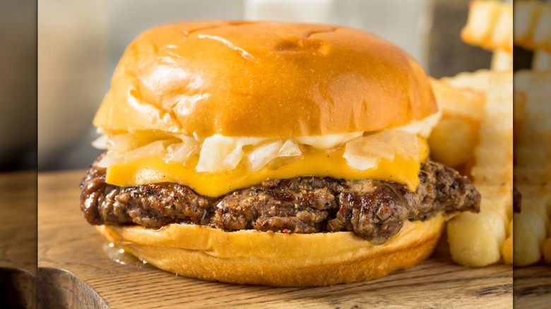 Close-up of a cheeseburger with chopped onions, melty cheese, and a single smashed patty on a bun