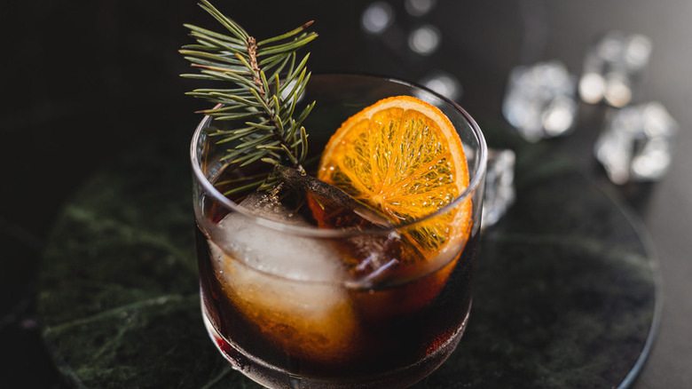 Bourbon cocktail in glass with orange slice and pine branch