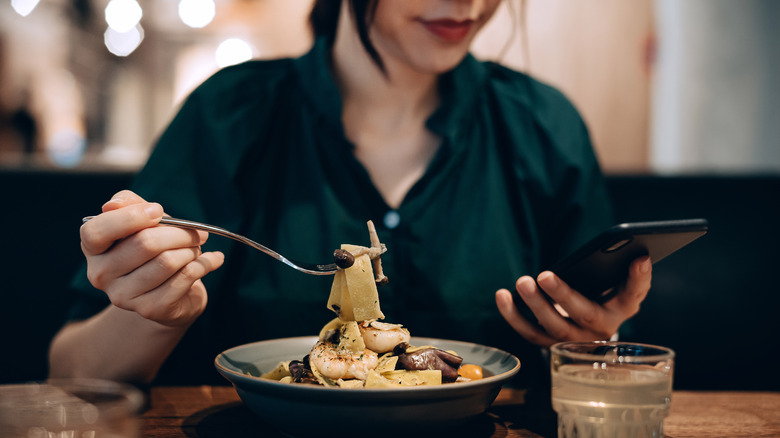 Someone eating pasta in a restaurant while looking at their phone