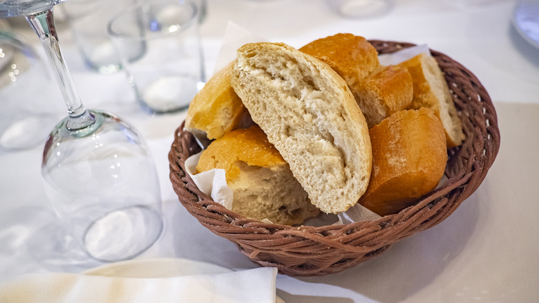 A bread basket placed on a restaurant table next to an upside down wineglass