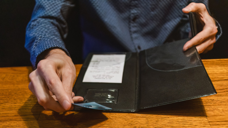 Someone holding a credit card while reviewing the bill at a restaurant