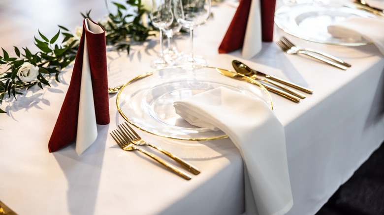 A white table napkin placed on a formal table setting with gold cutlery