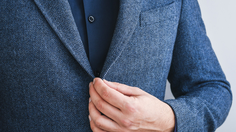 A person fastening the button on a blue tweed suit