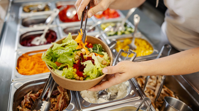 Hands making salad in a bowl from a salad buffet
