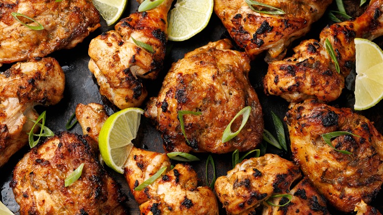 Close up of jerk chicken pieces with lime wedges and chopped green onion