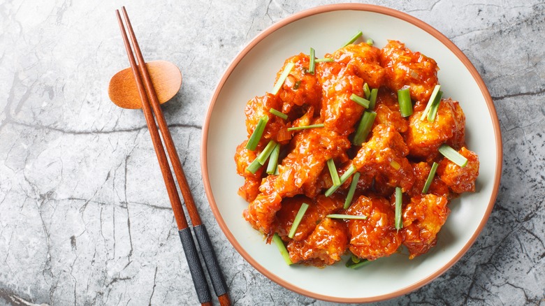 Crispy cauliflower in sticky spicy sauce on plate next to chopsticks