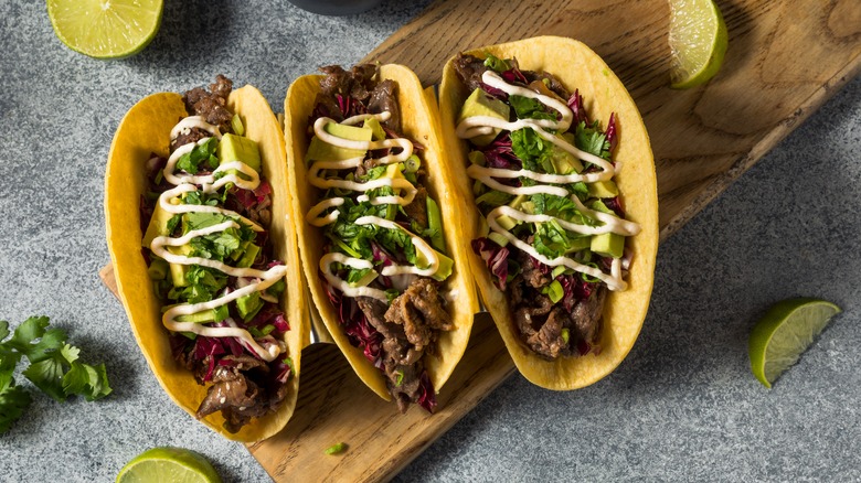 Three bulgogi beef tacos on wooden board with lime wedges