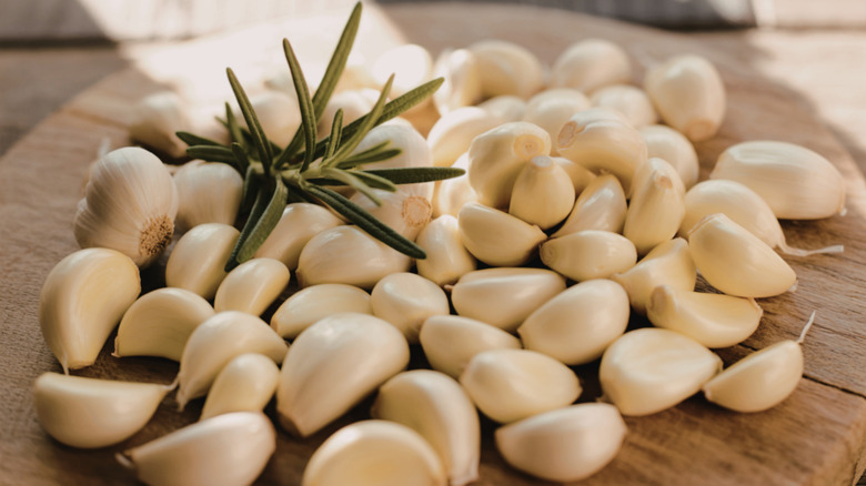 Peeled garlic and rosemary sprig on wooden cutting board
