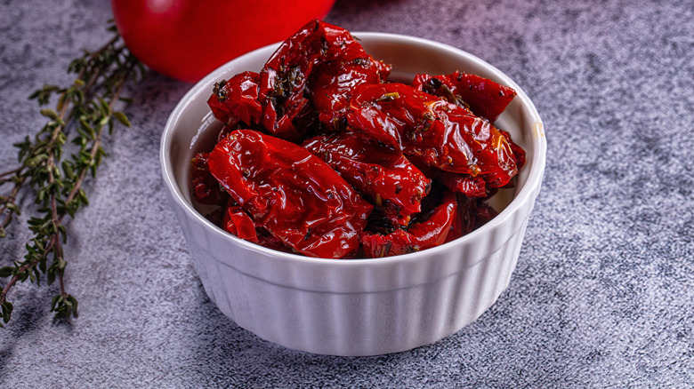 White ramekin with sun dried tomatoes on grey surface, thyme beside