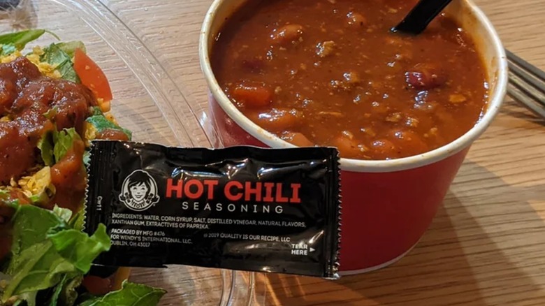 Packet of Wendy's hot chili seasoning in between a taco salad and bowl of chili