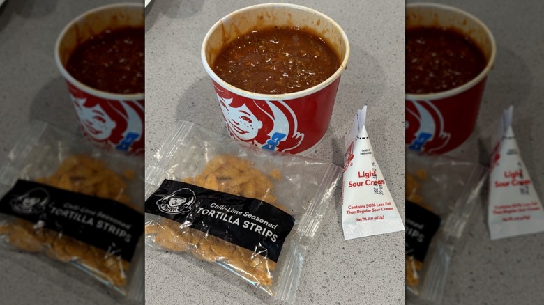 Paper bowl of Wendy's chili with package of chili-lime seasoned tortilla strips and light sour cream packet