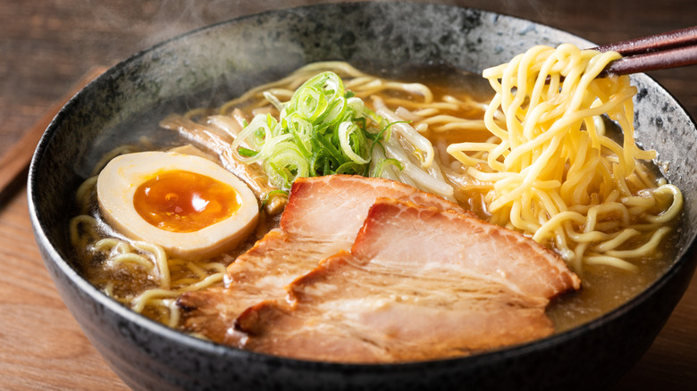 Chopsticks lifting noodles from steaming bowl of ramen