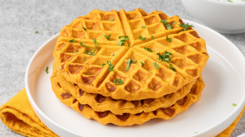 Stack of three sweet potato waffles on plate, topped with chopped green herbs