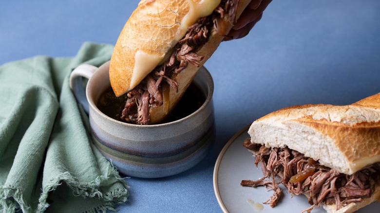 Dipping French dip sandwich into mug of gravy