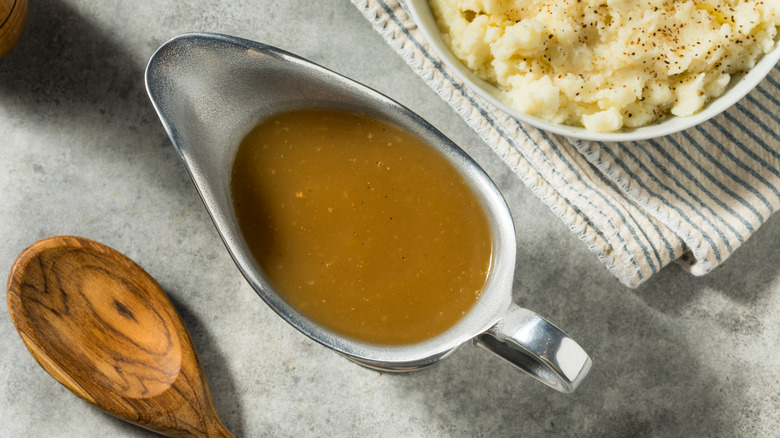 Gravy in gravy boat next to wooden spoon and bowl of mashed potatoes