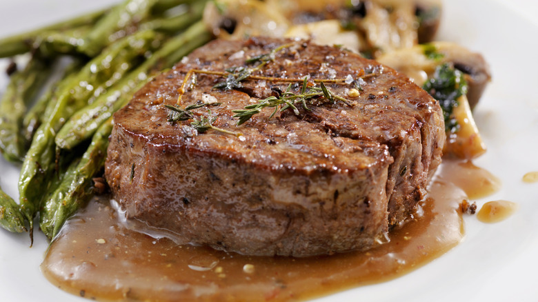 Steak with gravy and green beans, topped with rosemary sprigs