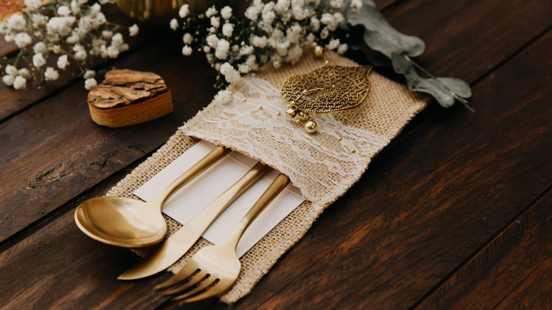 Golden cutlery placed in burlap pocket in a rustic setting against a wooden table