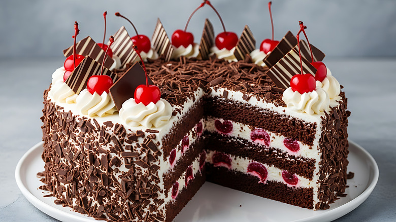 Sliced black forest cake on plate, topped with whipped cream, chocolate shards, and candied cherries