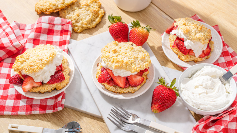Strawberry shortcake desserts on plate, next to fresh strawberries and bowl of whipped cream