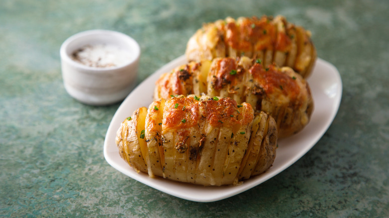 Three cheesy hasselback potatoes on white plate