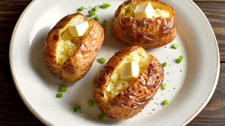 Three baked potatoes on plate, split open and topped with butter