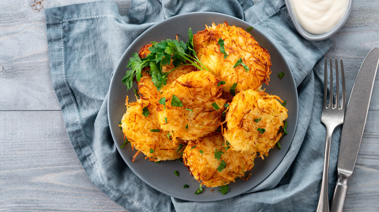 Pile of crispy hash browns on plate with fresh herbs