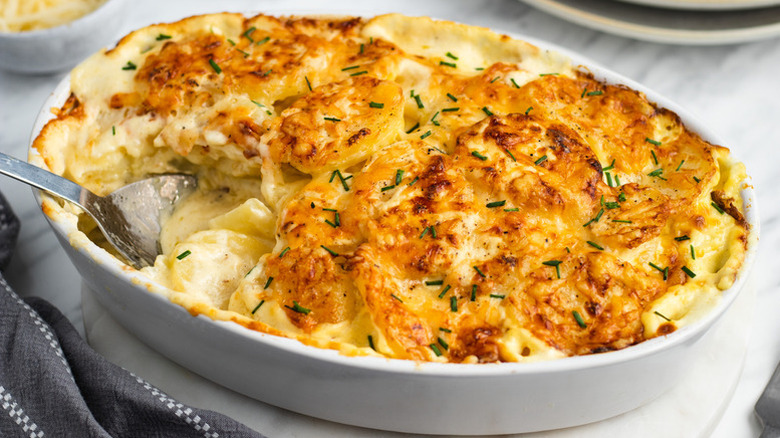 Cheesy potato gratin in baking dish with spoon