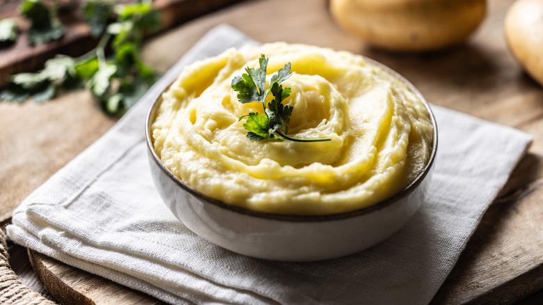 Bowl of mashed potatoes garnished with sprig of parsley