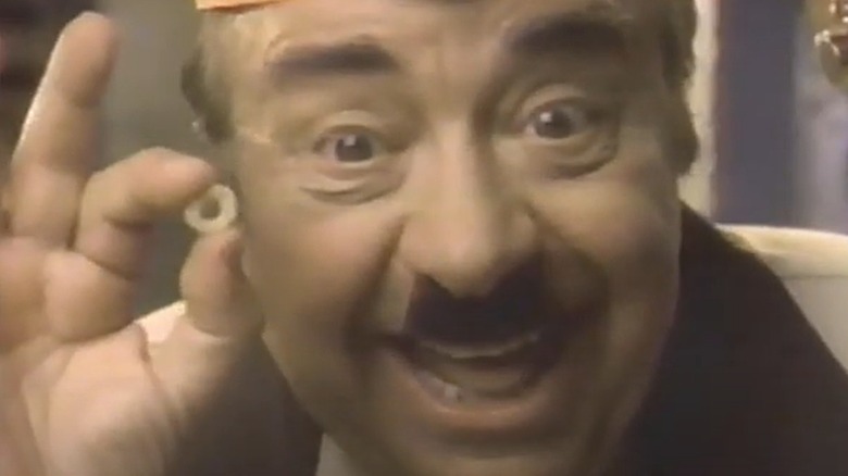 A close up of Fred the Baker in an old commercial holding a cereal piece that looks like a mini donut