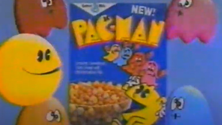 A still image from an '80s TV commercial featuring a box of Pac-Man cereal on a blue background surrounded by cartoon characters