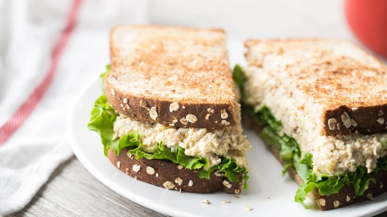 Chicken salad sandwich on plate sitting on a table top next to napkin