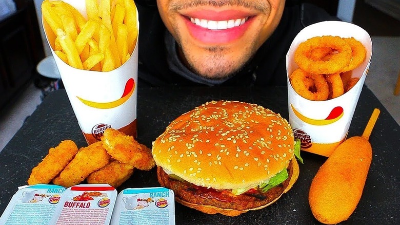 Tray of Burger King food, including fries, onion rings, Impossible Whopper, and corn dog, with person's smile.