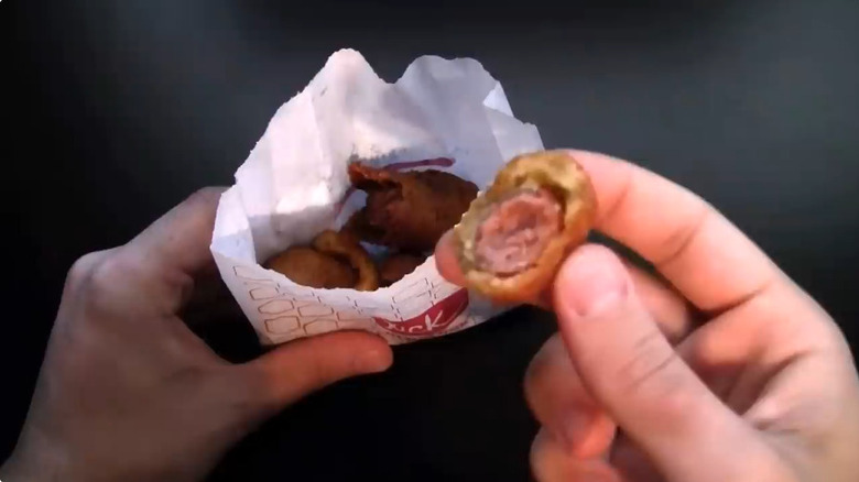 Screenshot of hands holding bag of Jack in the Box Mini Corn Dogs, one with a bite taken out of one.