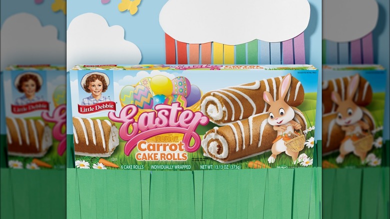 Little Debbie Easter Carrot Cake rolls box against paper grass and paper clouds/rainbow background