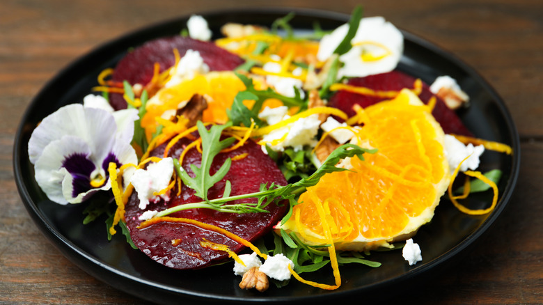 A beet and orange salad served on a black plate with arugula and floral garnishes