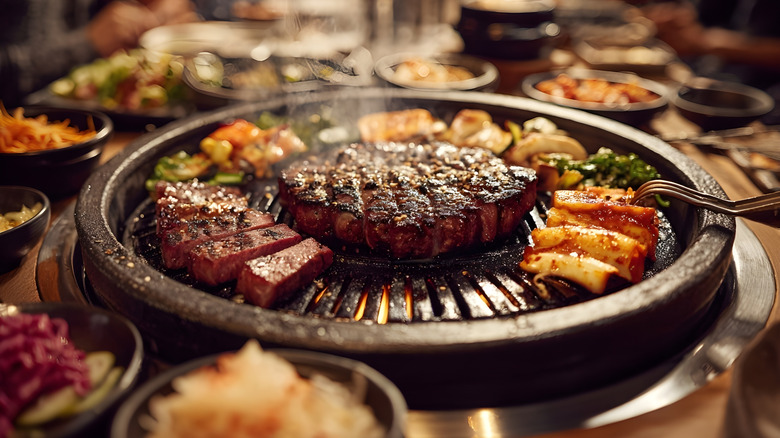 Meat grilling on a Korean BBQ surrounded by classic Korean sides