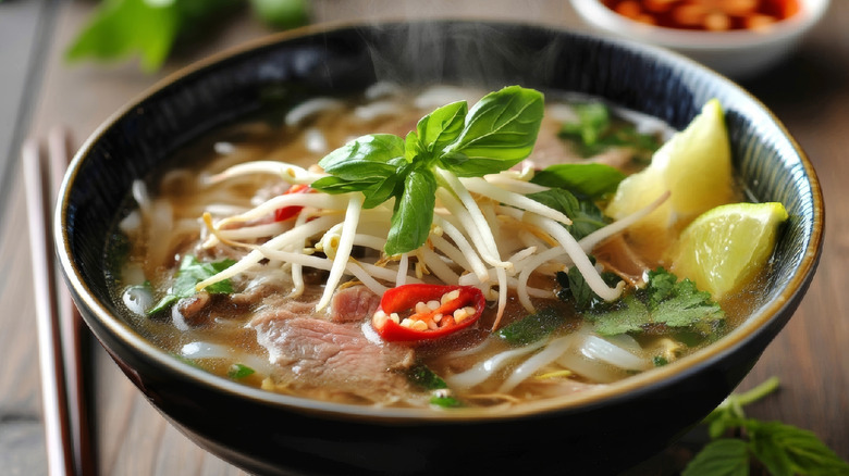 A hot bowl of Pho topped with sprouts, chili peppers, lime, and greens